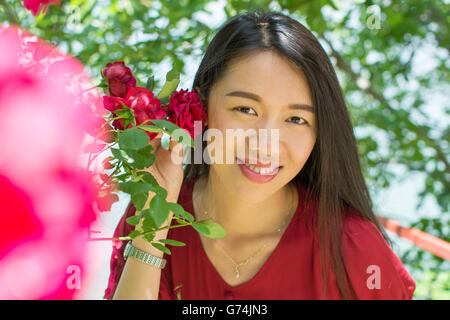 Donna in abito rosso tenendo una rosa rossa vicino al suo viso Foto Stock