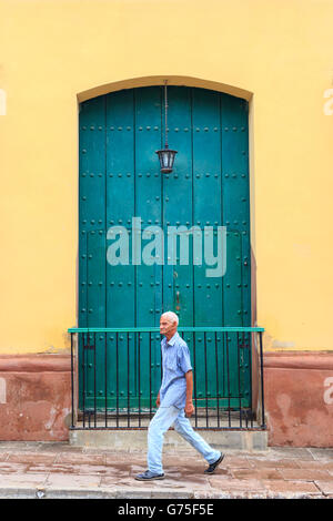 Uomo cubano camminando passato tradizionale verde porta di legno di una tipica casa coloniale,Trinidad, Cuba, un sito Patrimonio Mondiale dell'UNESCO Foto Stock