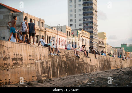 La gente seduta sulla parete del mare di fronte al Malecon (strada costiera) in Havana, Cuba Foto Stock