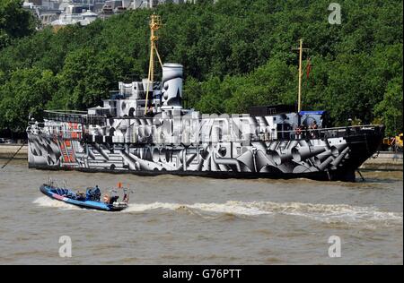 Una barca da diporto passa dalla nave da guerra della prima guerra mondiale, il presidente HMS (1918), che è diventata un'opera d'arte pubblica sull'argine di Londra, chiamata Dazzle Ship London dall'artista Tobias Rehberger, la nave, una delle ultime tre navi da guerra della prima guerra mondiale, È stato coperto in stampa camouflage abbagliante come parte di 14 - 18 ora, un programma di eventi per celebrare il centenario della prima guerra mondiale Foto Stock