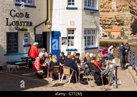 Regno Unito, Inghilterra, Yorkshire, Staithes, High Street, i clienti seduti ai tavoli nella luce del sole al di fuori Cod & Lobster pub Foto Stock
