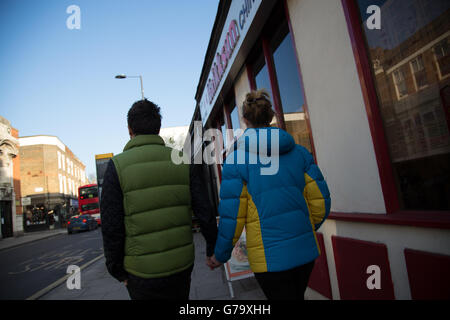Uomo in verde puffer giacca donna in blu e giallo puffer giacca da dietro, Stoke Newington, Londra. Foto Stock