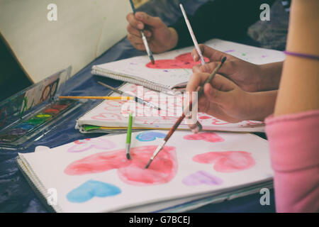 Fotografia di alcune mani con pennelli pittura cuori Foto Stock