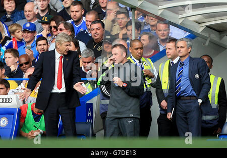 Arsenal manager Arsene Wenger (a sinistra) in discussione con il quarto ufficiale Jon Moss (al centro) sulla linea di contatto come il manager del Chelsea Jose Mourinho (a destra) guarda avanti durante la partita della Barclays Premier League a Stamford Bridge, Londra. Foto Stock