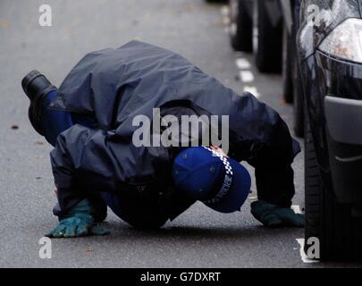 Un poliziotto cerca sotto un'auto all'interno di una zona cordonata fuori di una casa in Airedale Avenue, Chiswick, dove un uomo è stato pugnalato a morte quando ha catturato un ladro rubando la sua casa. Foto Stock