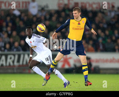 Bafetimbi Gomis di Swansea City (a sinistra) e Arsenal's per Mertesacker combattono per la palla durante la partita della Barclays Premier League al Liberty Stadium di Swansea. Foto Stock