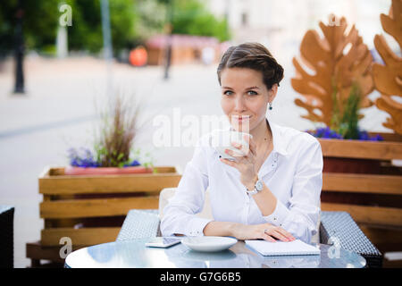 Pausa caffè. Attraente giovane imprenditrice nel convenzionale sorridere mentre in seduta cafè sul marciapiede e di bere il caffè. Foto Stock