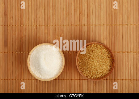 La scelta, la selezione dei due zuccheri in piccole ciotole di legno sul tappetino di bambù sfondo, marrone e canna da zucchero bianco, vista dall'alto Foto Stock