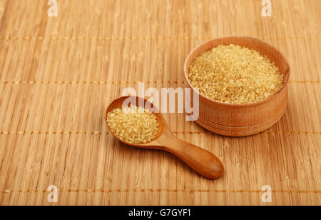 Rotonda di Legno cucchiaio e una piccola ciotola di marrone zucchero di canna sul tappetino di bambù sfondo Foto Stock