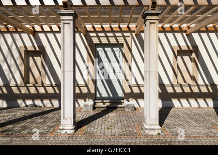 Vista frontale sul lato ingresso di una vecchia villa con una pergola. La forte luce solare getta ombra scura su strisce l'edificio Foto Stock