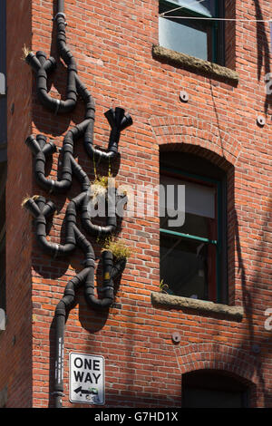 Pioggia nera tubi di gronda fissato in un intricato e modo insolito di un rosso-marrone di un muro di mattoni Foto Stock