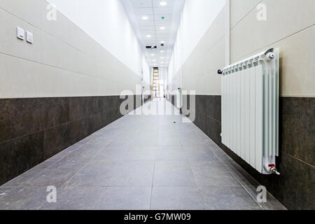 Radiatore bianco a lungo stretto corridoio con parete di piastrelle e pavimento. Foto Stock