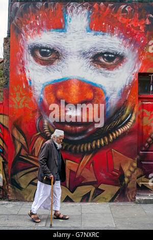 Un anziano uomo asiatico passeggiate da un pezzo di arte di strada da Dale Grimshaw in Hanbury Street, appena fuori la Brick Lane, Londra. Foto Stock