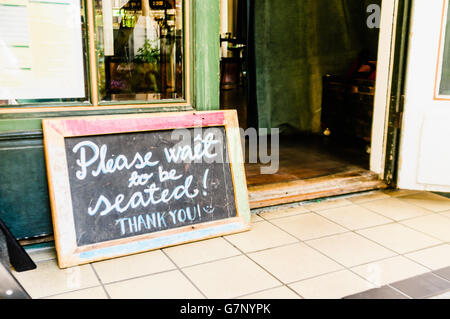 Segno al di fuori di un ristorante dicendo "Si prega di attendere di essere seduti! Grazie!" Foto Stock