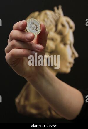 Un assistente dell'evento della zecca reale tiene una nuova moneta da due libbre davanti al ritratto di coniazione di Arnold Machin della regina Elisabetta II durante una cerimonia di inaugurazione dell'ultimo ritratto di coniazione della regina Elisabetta II alla National Portrait Gallery di Londra. Foto Stock
