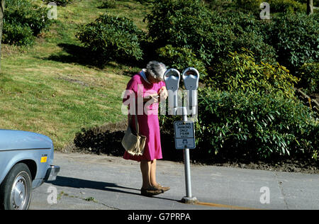 Donna anziana ottenere le monete al di fuori della sua borsa per pagare il parcheggio metro Foto Stock