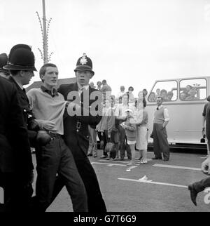 Ufficiali di polizia in uniforme che tengono un giovane a Hastings, Sussex, dopo un incidente che ha coinvolto un'automobile della berlina della famiglia. La polizia supplementare, 69 volati dalla forza metropolitana, è stata portata ad Hastings dopo sporadici focolai di guai. Mods e Rockers scesero in città, per lo più da scooter e moto, ma alcuni anche in treno. Foto Stock