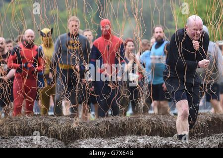 Un partecipante corre attraverso la "elettroshock Therapy" mentre quattro uomini vestiti come supereroi guardano durante il duro Mudder London West a Culden FAW a Henley-on-Thames, Oxfordshire. Foto Stock