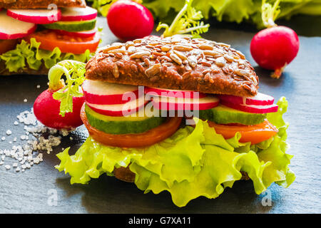 Veggie hamburger (insalata verde, fresco cetriolo, pomodoro, il ravanello) e ravanelli su sfondo scuro. Foto Stock