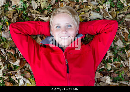 Giovane donna sdraiata su foglie di autunno Foto Stock