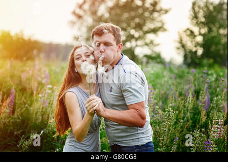 Giovane coppia felice soffiando insieme di tarassaco, outdoor in natura Foto Stock