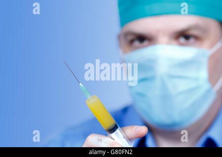 Maschio adulto medico con il cappuccio e la maschera tenendo la siringa con il giallo vaccina nelle sue mani Foto Stock