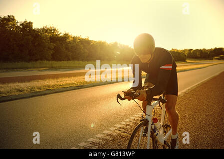 Riflessi di luce di salire o di sole che tramonta sull uomo del training su strada solo in bici su strada asfaltata in estate Foto Stock