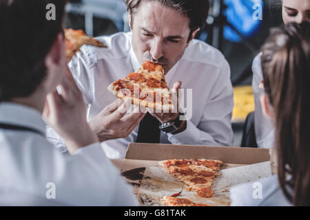 Il team Aziende di mangiare la pizza in ufficio seduti attorno al tavolo Foto Stock