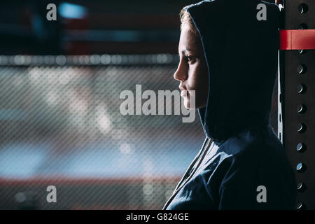 Close-up vista laterale della donna che indossa maglietta con cappuccio in piedi alla palestra Foto Stock