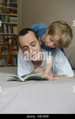 Padre e figlio libro lettura mentre giaceva sul letto di casa Foto Stock