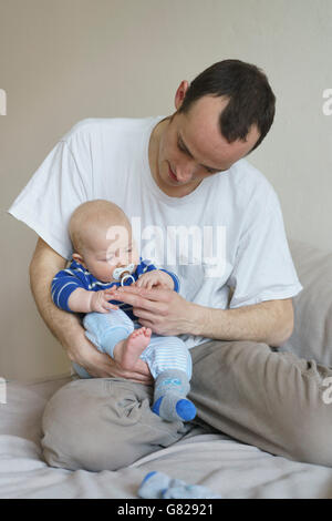 Vista frontale del padre che porta il figlio mentre è appoggiato sul letto di casa Foto Stock