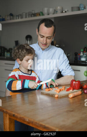 Padre guardando il figlio carota spacco sul tavolo in cucina Foto Stock