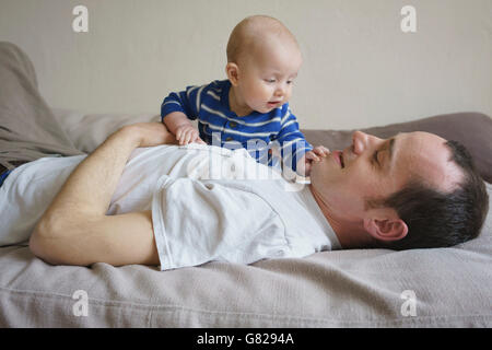 Vista laterale del padre giaceva con figlio sul letto di casa Foto Stock