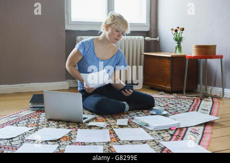Giovane donna facendo scartoffie mentre è seduto a casa Foto Stock