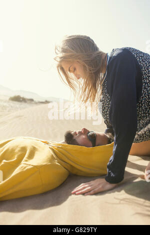 Vista laterale della romantica giovane donna guardando uomo disteso sulla sabbia Foto Stock