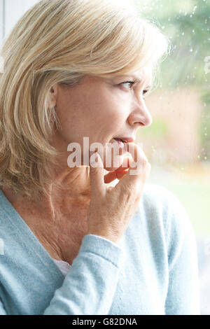 Triste donna matura che soffrono di agorafobia guardando fuori della finestra Foto Stock