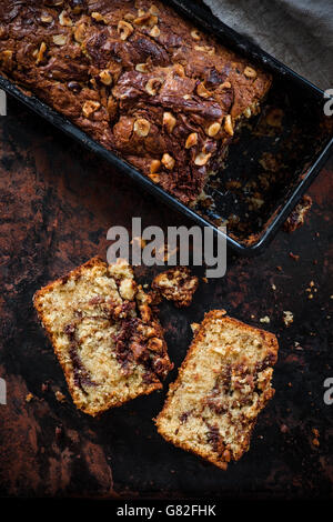 Vista superiore del pane alla banana con Nutella swirl e nocciole tritate su uno sfondo scuro. Cibo scure della fotografia. Foto Stock