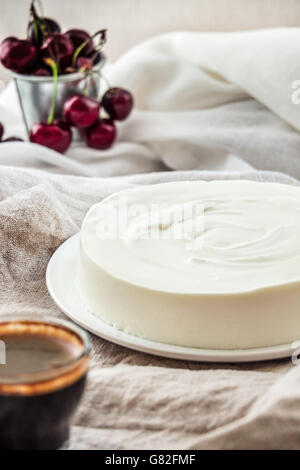 La vaniglia bavarese torta con crema di formaggio e panna montata. Piastra bianca. Le ciliegie sullo sfondo. Foto Stock