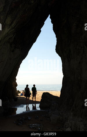 Uscendo da una grotta sulla spiaggia e due persone scoprono la meraviglia di Gower attraverso questo gateway naturale Foto Stock