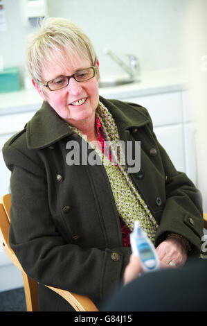 Bianco matura donna si siede nel suo cappotto durante un GP consultazione con il suo medico al GP di NHS health center al momento della ricezione di una buona notizia Foto Stock