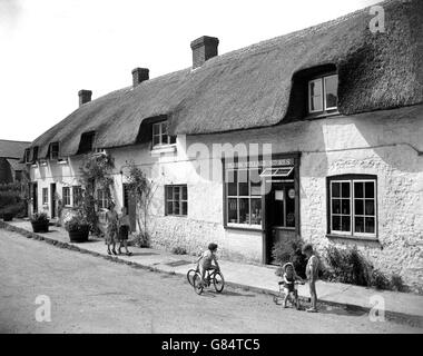 Bambini che giocano al sole da una fila di cottage con tetto di paglia e negozi di villaggio a Plush, Dorset. Il villaggio di 400 anni è venduto all'asta pubblica a Dorchester. Foto Stock