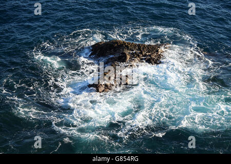 Corona di schiuma attorno ad una roccia nell'oceano Foto Stock