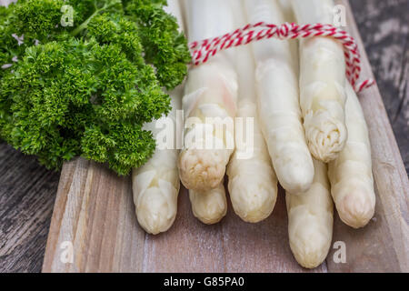 Bundle di asparagi bianchi con il prezzemolo un rustico in legno piastra Foto Stock