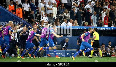 Inghilterra manager Roy Hodgson sconsolato in panchina come Islanda giocatori e staff correre sul Passo per celebrare la sua vittoria durante il Round di 16 corrispondono a Stade de Nice, Nice, Francia. Foto Stock