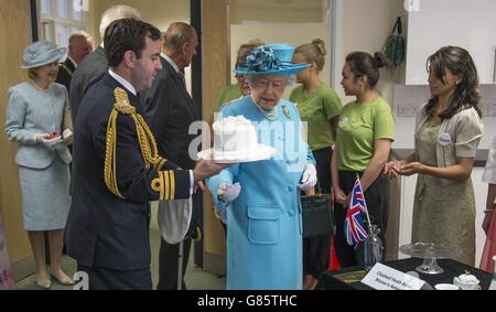 La regina Elisabetta II, accompagnata dal Duca di Edinbugh (non nella foto) viene presentata con una torta da un gruppo asiatico delle donne e la passa Equerry Andrew canale durante la sua visita al Chadwell Heath Community Center dove ha incontrato residenti locali di tutte le età che utilizzano la struttura. Foto Stock