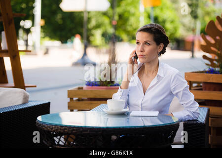 Buon business talk. Allegro giovane imprenditrice parlando al telefono cellulare e la coppa di ritegno di caffè seduti all'aperto Foto Stock