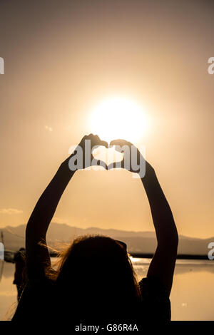Donna messa a forma di cuore con le mani al tramonto Foto Stock