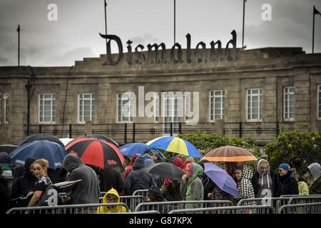 Le persone si accodano sotto la pioggia per acquistare i biglietti per il parco a tema "Dismaland" di Banksy a Weston-super-Mare, Somerset. Foto Stock