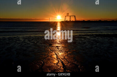 Il sole d'autunno sorge sul mare del nord di fronte alla coppia dell'artista Sean Henry a Newbiggin-by-the-Sea, Northumberland, come condizioni miste e notti più fredde sono in serbo per la Gran Bretagna dopo l'arrivo dell'equinozio d'autunno. Foto Stock