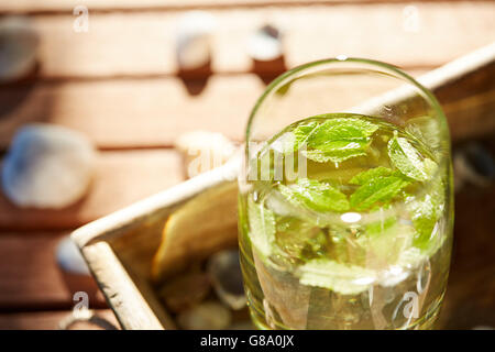 Avendo un bel drink fresco in un bicchiere con la menta e il ghiaccio su un tavolo di legno nel giardino in estate Foto Stock